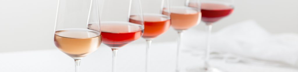 Grouping of five varieties of rose wine in wineglasses in a row.